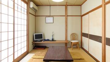 Una habitación tradicional japonesa con suelo de tatami, una mesa baja, una silla, un televisor y una lámpara colgante.