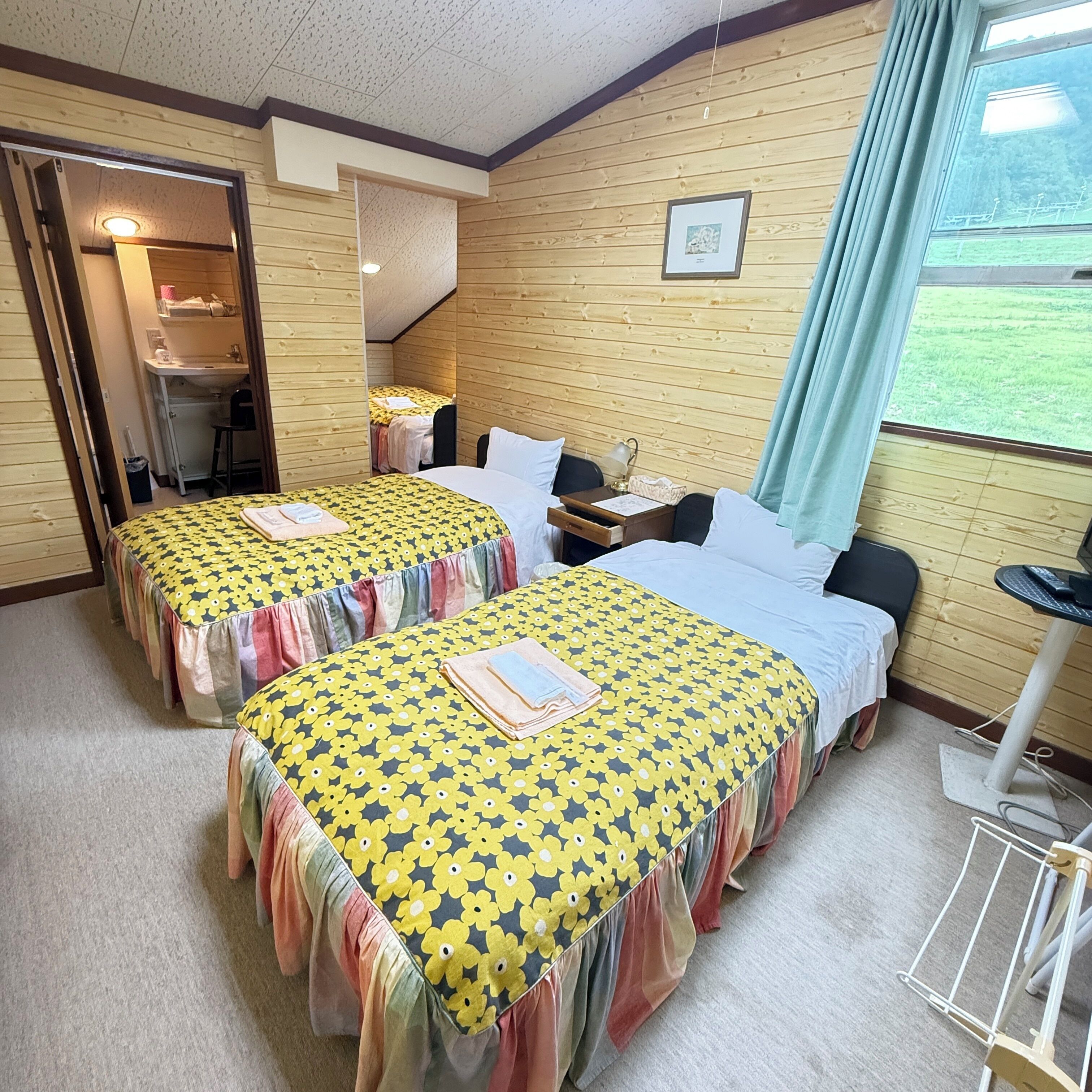 Quarto com duas camas, uma escrivaninha, uma cadeira, uma mesa pequena e uma janela com vista para o exterior.