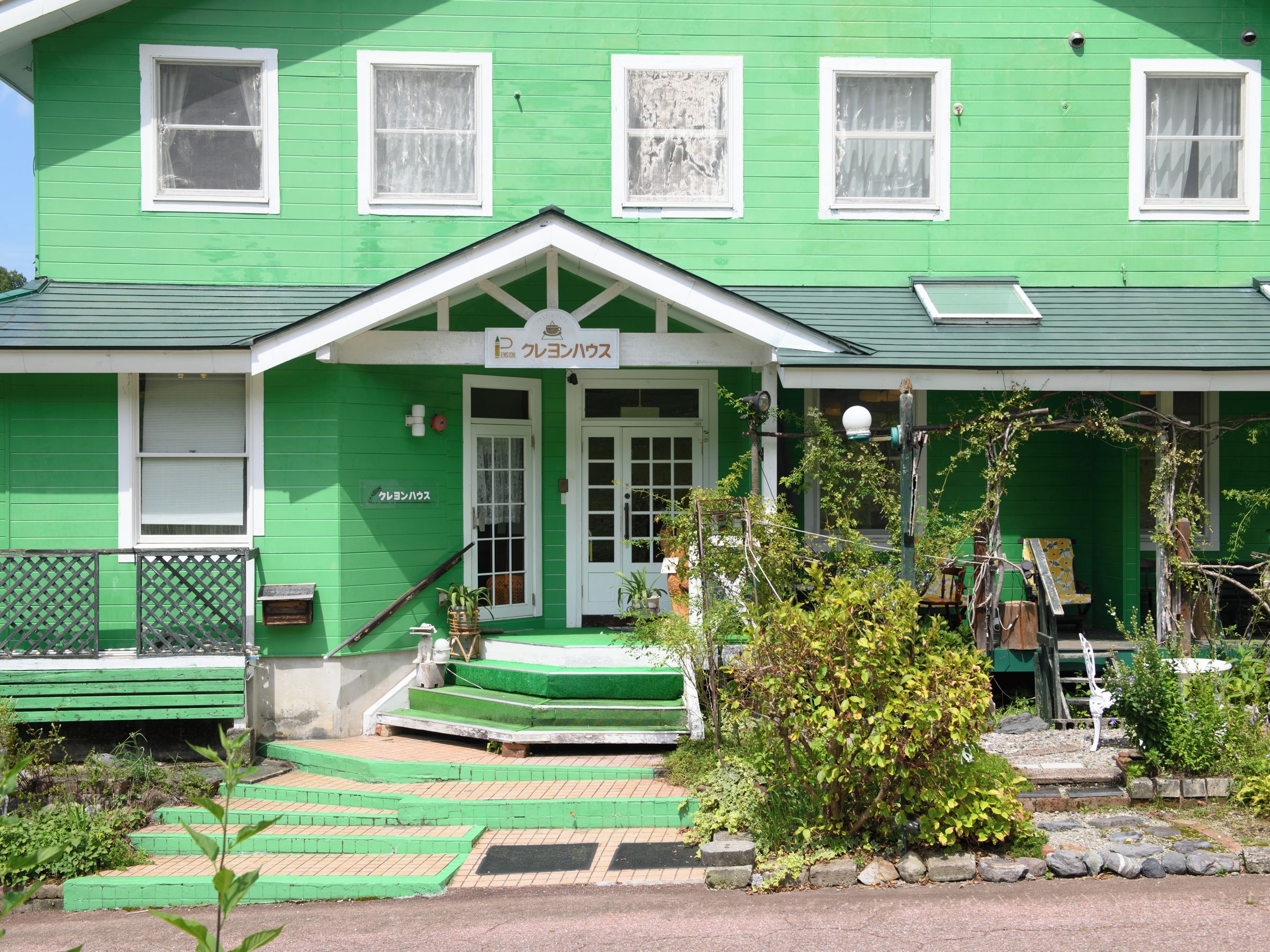 Un edificio verde con una puerta blanca y un letrero encima.