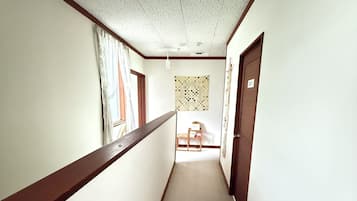 A corridor with a wooden handrail, a patterned wall hanging, and a door with a number sign.