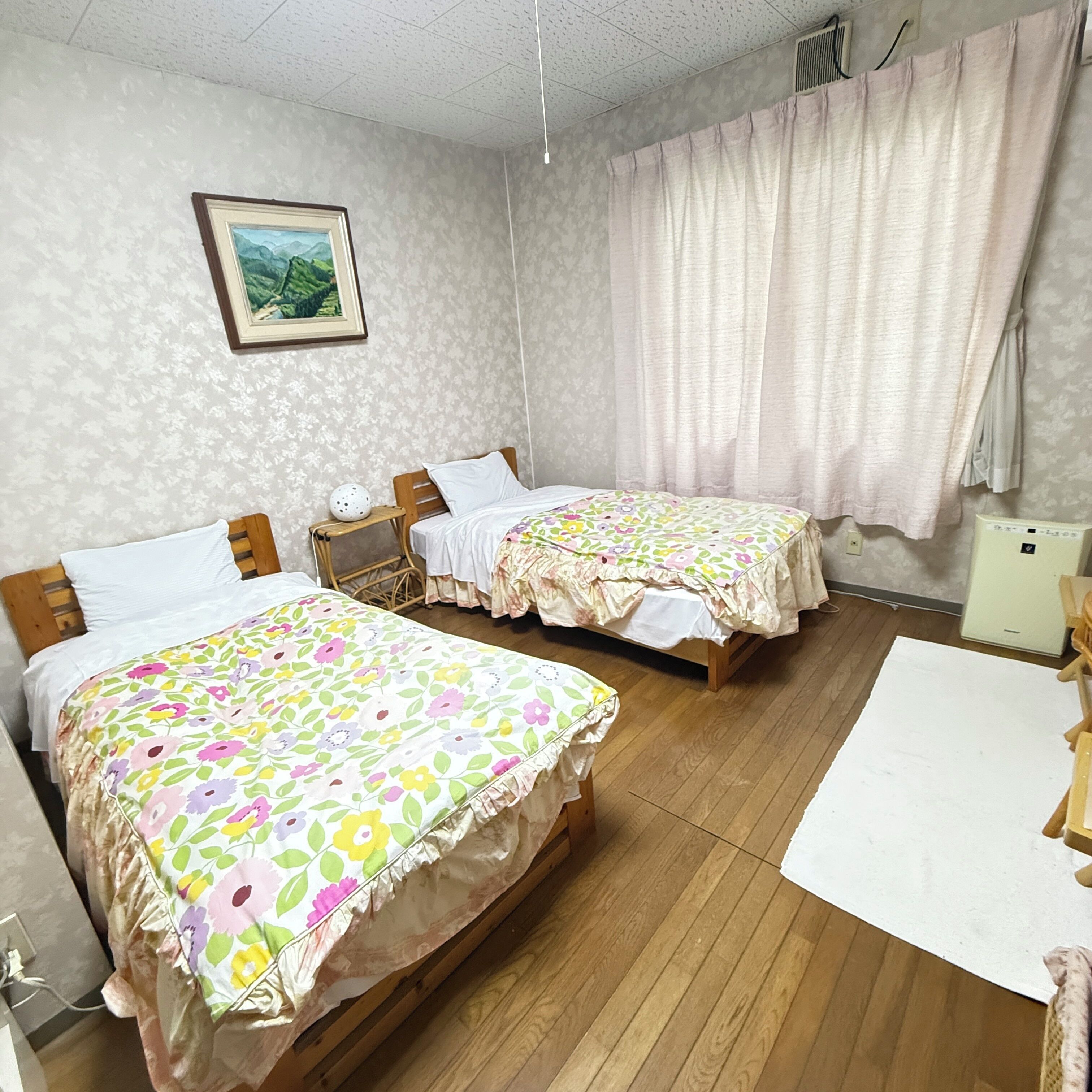 Habitación de hotel con dos camas, una mesita, una silla, un cuadro en la pared y una ventana con cortinas.