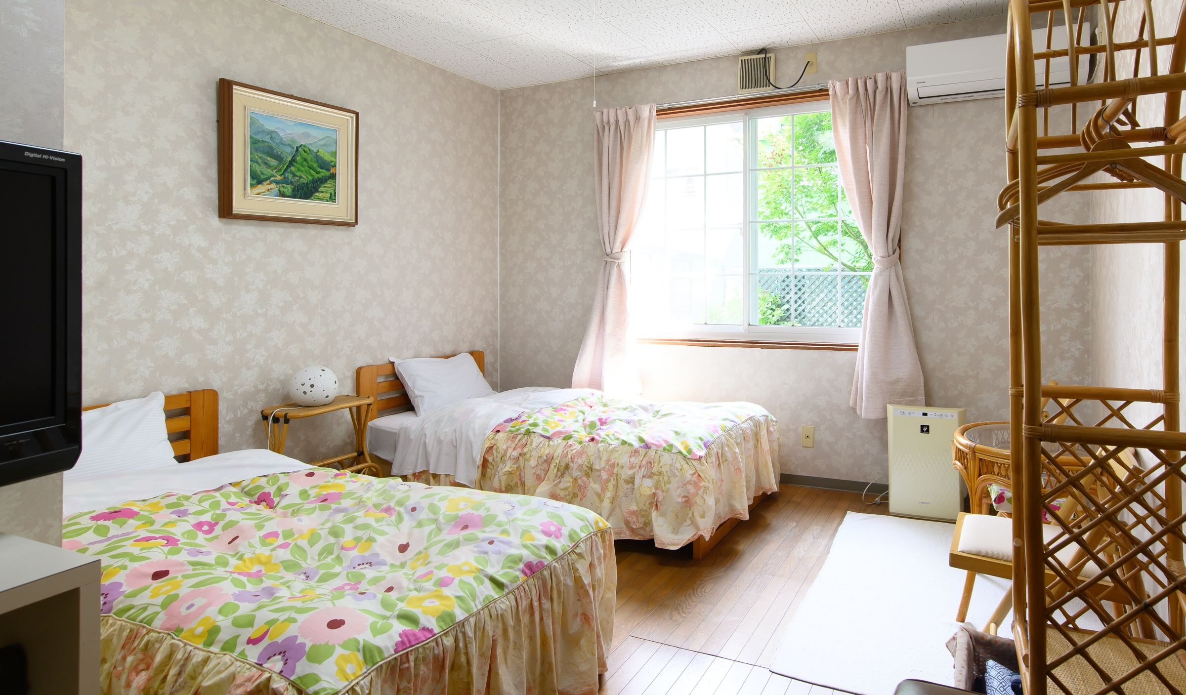 A room with two beds, a window with curtains, a wall-mounted air conditioner, and a television.