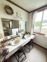 Un baño con dos lavamanos, un espejo, un reloj y una ventana con cortinas.