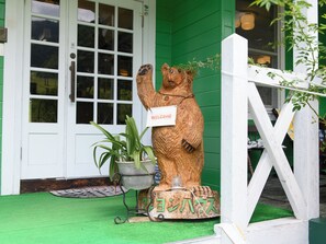 Una escultura de madera de un oso con un letrero que dice 'WELCOME', una planta en maceta y una base de madera con caracteres japoneses.