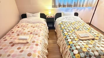 Habitación de hotel con dos camas individuales, una mesita de noche con lámpara y una ventana con cortinas.