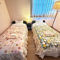 Habitación de hotel con dos camas individuales, una mesita de noche con lámpara y una ventana con cortinas.