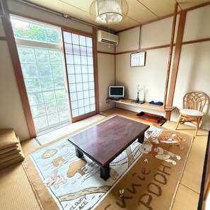 Um quarto japonês tradicional com tatames, uma mesa baixa, uma televisão e uma cadeira.