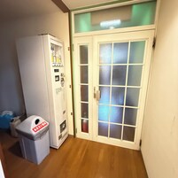 A room with a white vending machine, a trash bin, and a glass door with a frosted panel.