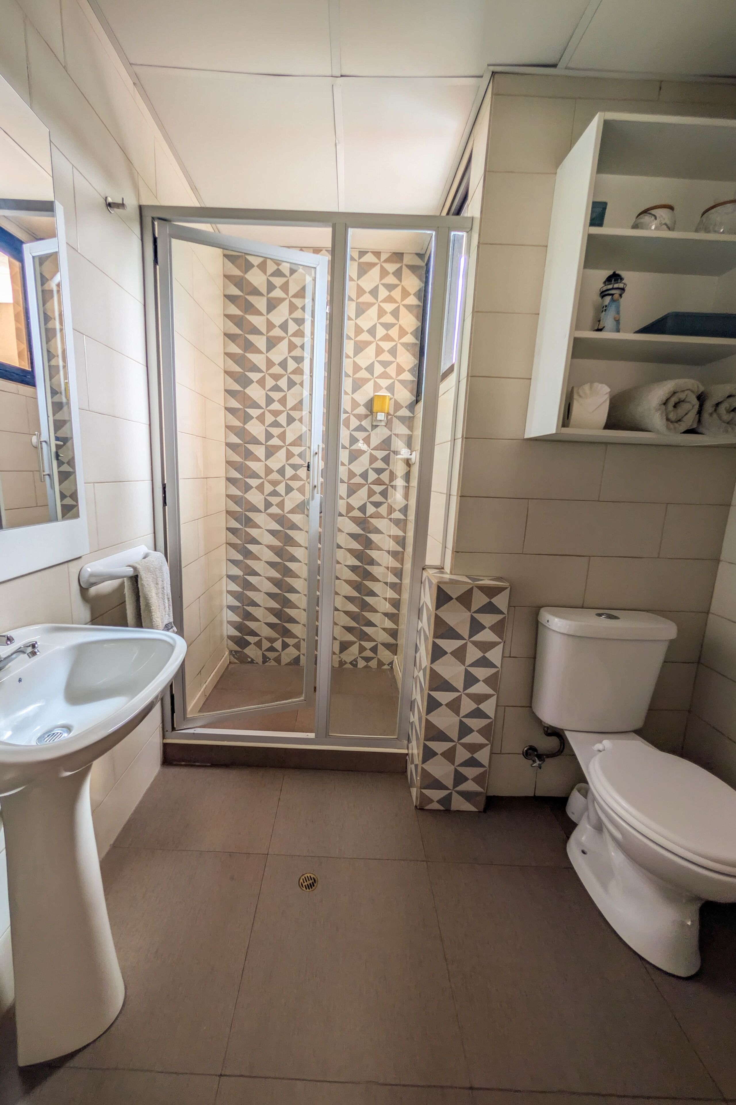 Une salle de bain équipée d’une douche, de toilettes, d’un lavabo et d’étagères où sont rangés les articles de toilette.