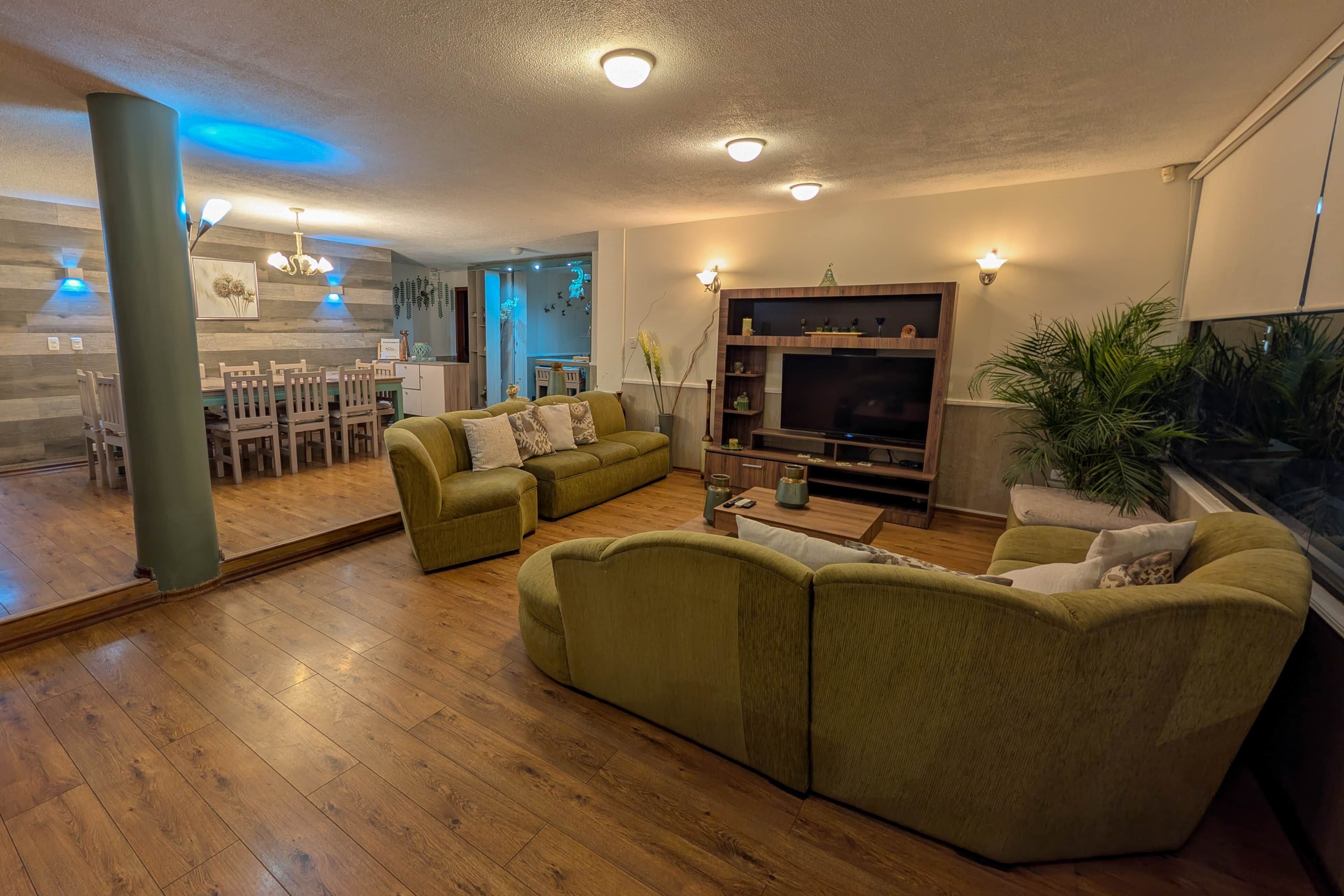 Uma sala de estar com sofá seccional, televisão e um espaço de jantar com cadeiras de madeira e mesa.