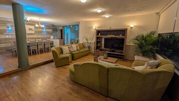 Una sala de estar con sofá seccional, televisor y comedor con sillas de madera y una mesa.
