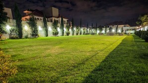 A well-lit outdoor area with a grassy lawn, surrounded by trees and buildings.