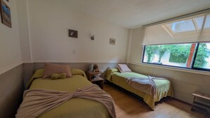 A room with two beds, a small table, and a window with a view of greenery.