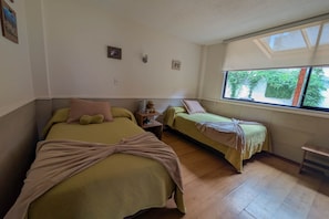 A room with two beds, a small table, and a window with a view of greenery.
