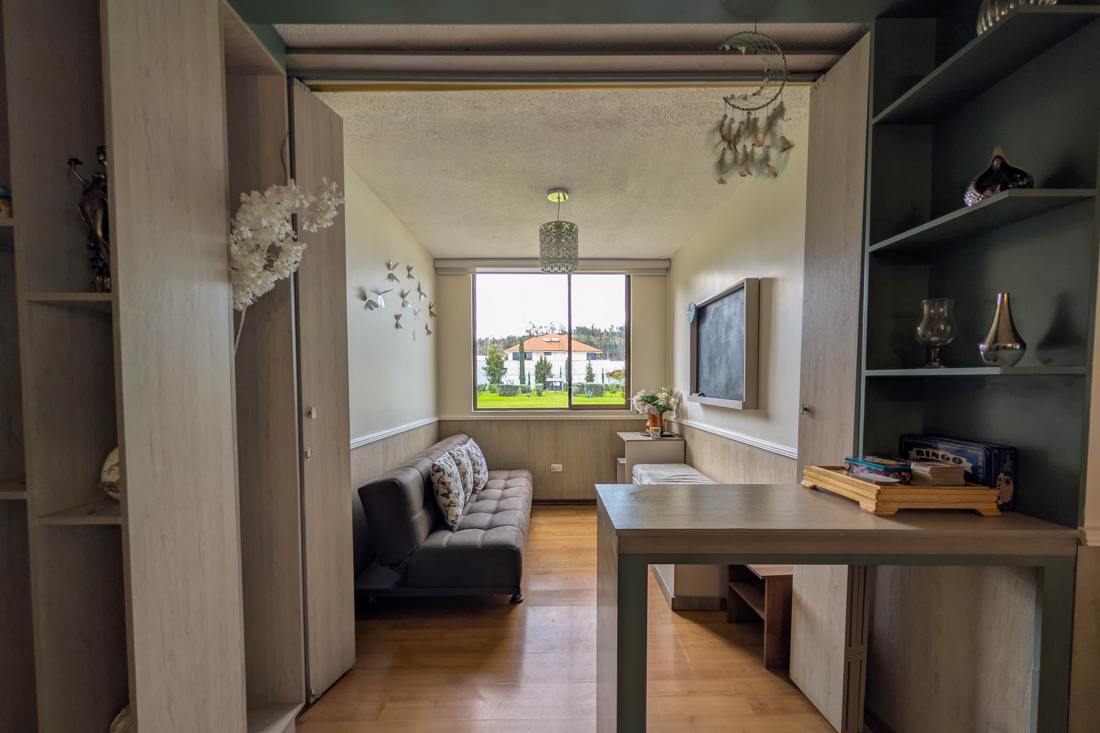 Un salon moderne avec un canapé, une table à manger et une vue dégagée sur l’extérieur grâce à une grande fenêtre.
