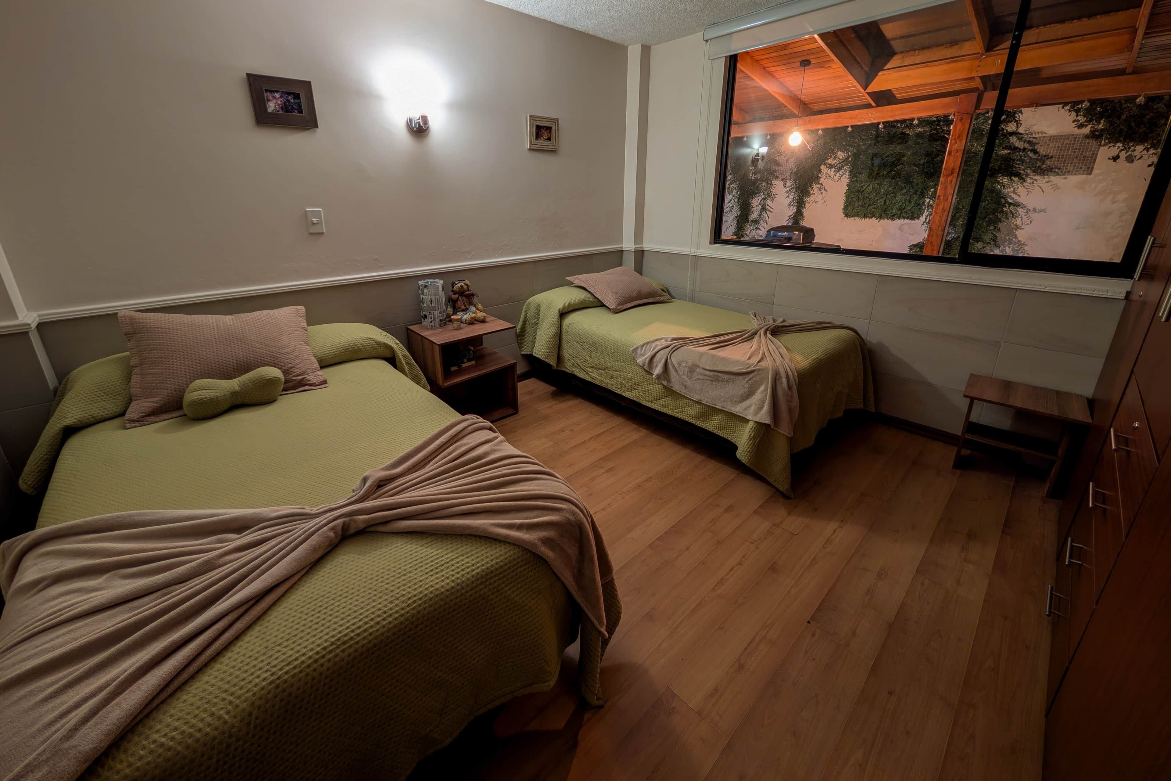 Une chambre avec deux lits simples, une petite table, une fenêtre donnant sur un paysage agréable et un plancher en bois.