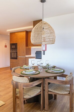 A dining area with a round wooden table set for four, surrounded by wicker chairs. - Wave 2.1 • Design and Conforto junto à Praia com AC (Vila Nova de Gaia)