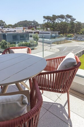 A balcony with wicker furniture and a view of a modern building and road. - Wave 2.1 • Design and Conforto junto à Praia com AC (Vila Nova de Gaia)