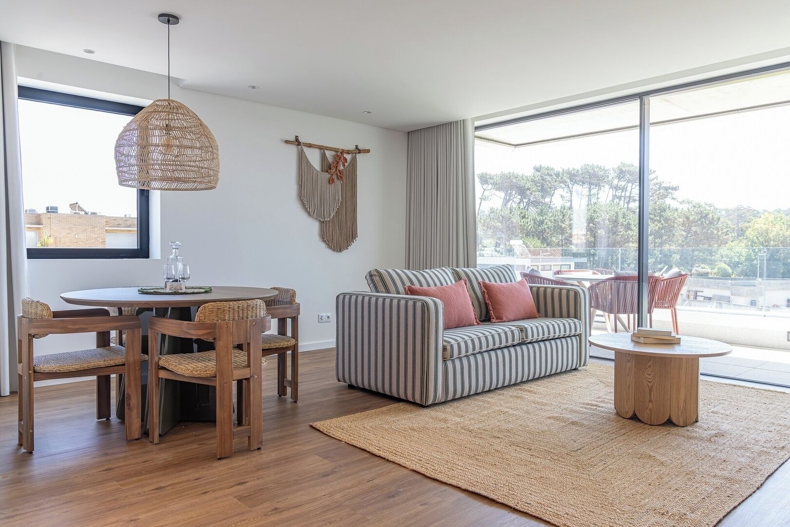 A modern living room with a round wooden table, striped sofa, and a woven hanging light fixture.