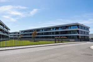 A modern multi-story building with a flat roof, large windows, and a black fence surrounding a green lawn. - Wave 2.1 • Design and Conforto junto à Praia com AC (Vila Nova de Gaia)