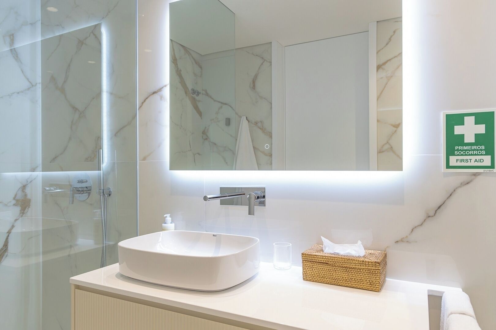A modern bathroom with a large mirror, a white sink, and a first aid sign.