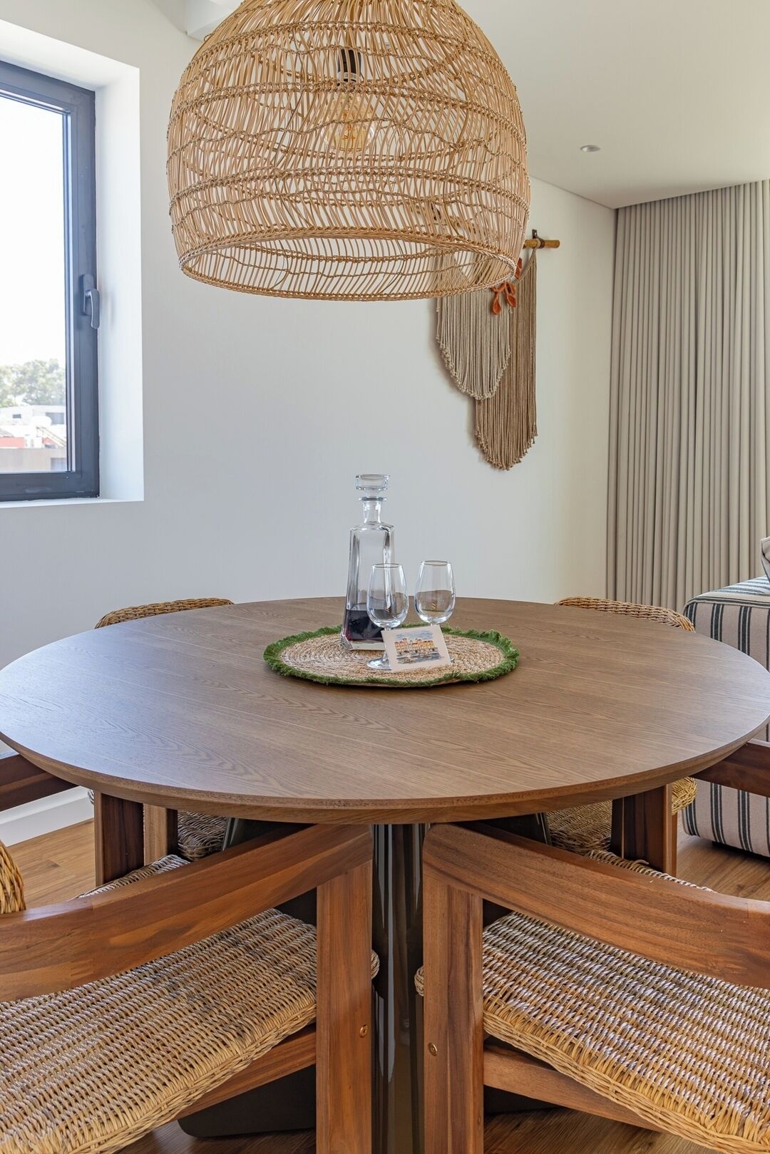A round wooden dining table with a woven centerpiece, surrounded by wicker chairs.