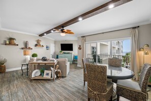 Amplia sala de estar con ventilador de techo, piso de madera y un balcón con mobiliario exterior.