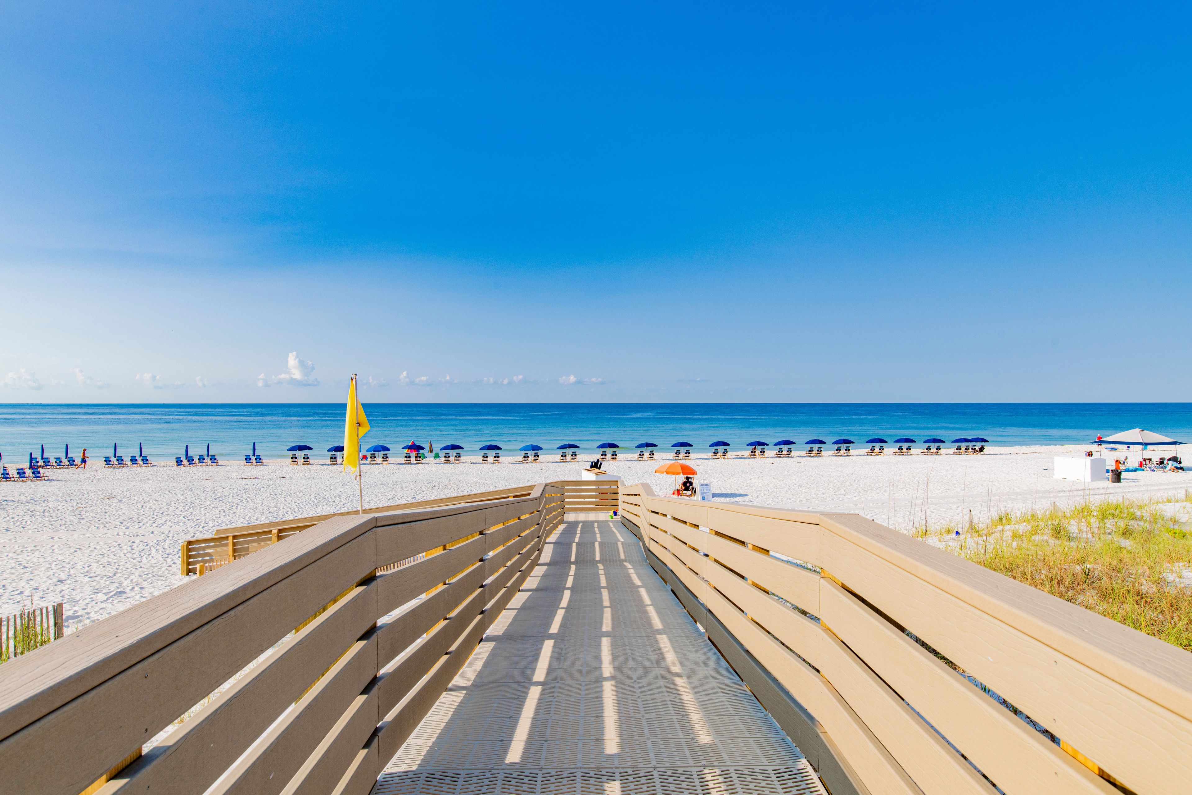 A wooden boardwalk leading to a beach with rows of sun loungers and umbrellas.