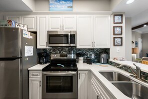 Una cocina moderna con armarios blancos, electrodomésticos de acero inoxidable, un microondas, horno y cafetera.
