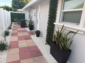 Ein Weg führt zu einem Gebäude mit weißer Fassade, einem grünen Heckenstreifen und Kübelpflanzen.
