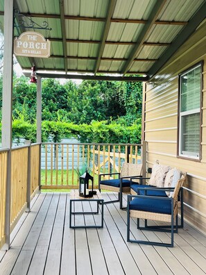 A covered porch with a sign reading 'The Porch Sit & Relax,' wooden deck, wicker furniture, and a view of a green landscape. - Little Piece of Paradise (Tampa)