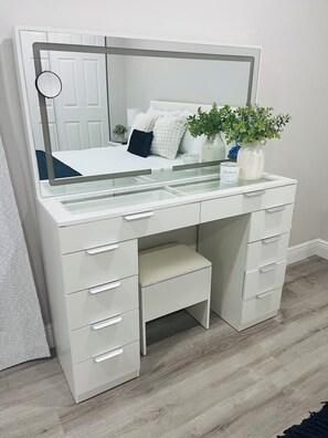 A white vanity with a mirror, drawers, and a shelf with a plant and a candle. - Little Piece of Paradise (Tampa)