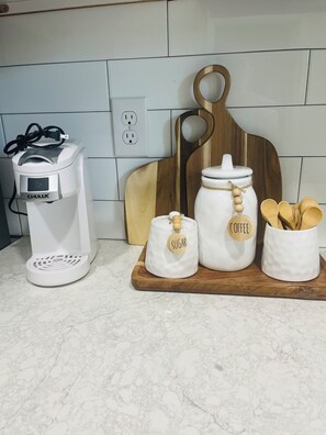 A kitchen counter with a coffee maker, a wooden cutting board, and two white containers with wooden labels for sugar and coffee. - Little Piece of Paradise (Tampa)