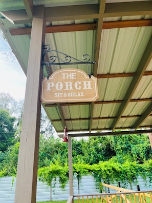 A wooden sign hanging from a metal structure with the words 'THE PORCH SIT & RELAX' written on it. - Little Piece of Paradise (Tampa)