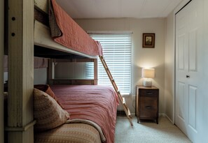 A room with a bunk bed, a bedside table with a lamp, a window with blinds, and a door. - Float down Muskegon River - Muskegon River Cottage (Grant)