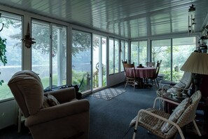 A sunroom with large windows, a dining table, chairs, a sofa, and a lamp. - Float down Muskegon River - Muskegon River Cottage (Grant)
