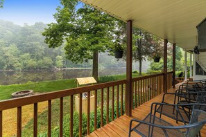 A wooden deck with outdoor seating, overlooking a lake and forested area. - Float down Muskegon River - Muskegon River Cottage (Grant)