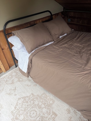A bed with a metal frame, brown bedding, and a white pillow.