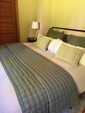 A bed with a quilted green cover, a wooden headboard, and multiple pillows. - Hillside retreat with modern finishes near Cooperstown and Oneonta (Oneonta)