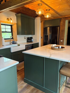 A kitchen with a large island, green cabinets, stainless steel appliances, and pendant lighting. - Hillside retreat with modern finishes near Cooperstown and Oneonta (Oneonta)