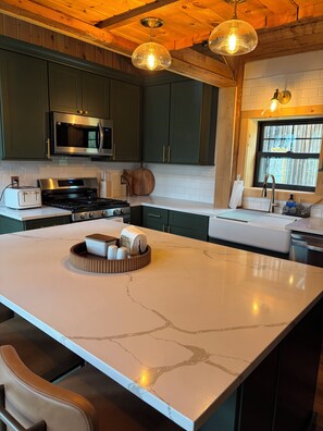 A kitchen with a large island, stainless steel appliances, and wooden ceiling beams. - Hillside retreat with modern finishes near Cooperstown and Oneonta (Oneonta)