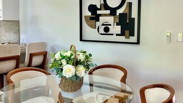 Un comedor con una mesa redonda de vidrio, sillas de madera, una lámpara colgante de fibras tejidas y una obra de arte abstracta enmarcada en la pared.
