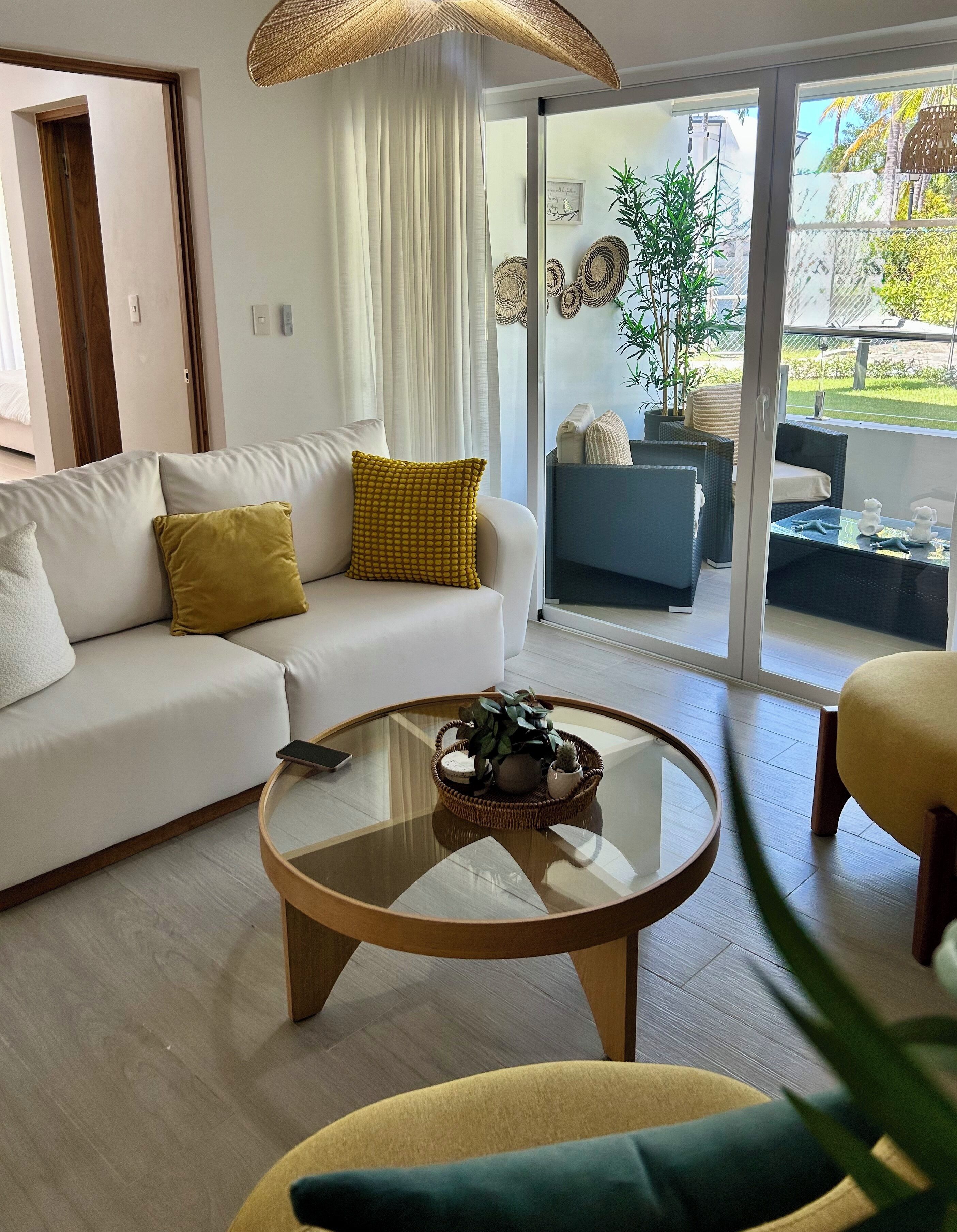 Una sala de estar moderna con un sofá, una mesa redonda de centro y vista a un jardín a través de amplios ventanales.