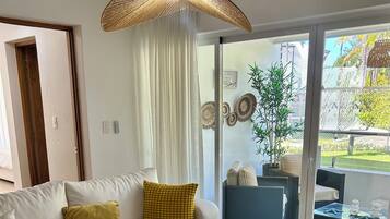 Una sala de estar moderna con un sofá, una mesa redonda de centro y vista a un jardín a través de amplios ventanales.