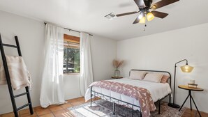 A bedroom with a bed, a ceiling fan, a window with curtains, a bedside table, and a floor lamp. - Hacienda Verde Spanish Style Home in the RGV (Weslaco)