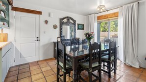 A dining area with a glass table and wooden chairs, a decorative mirror, and a view of the outdoors through a window with curtains. - Hacienda Verde Spanish Style Home in the RGV (Weslaco)