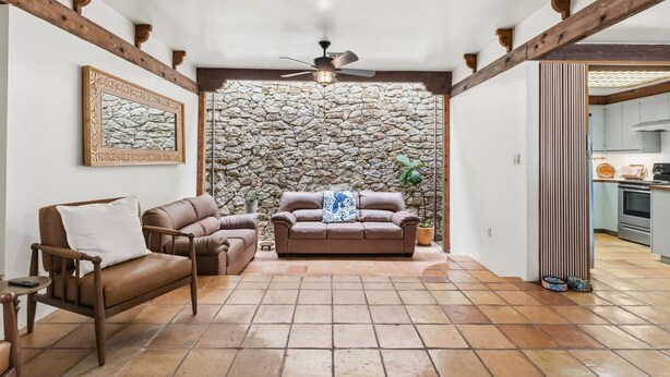 A living room with a stone wall, two sofas, a ceiling fan, and a kitchen visible through an open doorway. - Hacienda Verde Spanish Style Home in the RGV (Weslaco)
