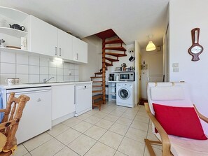 Una cucina compatta con mobili bianchi, una scala in legno, una lavatrice e un'area pranzo con un cuscino rosso.
