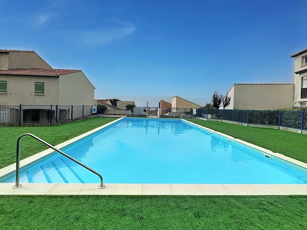 Una piscina rettangolare con una scaletta metallica su un lato, circondata da erba sintetica verde e una recinzione blu.