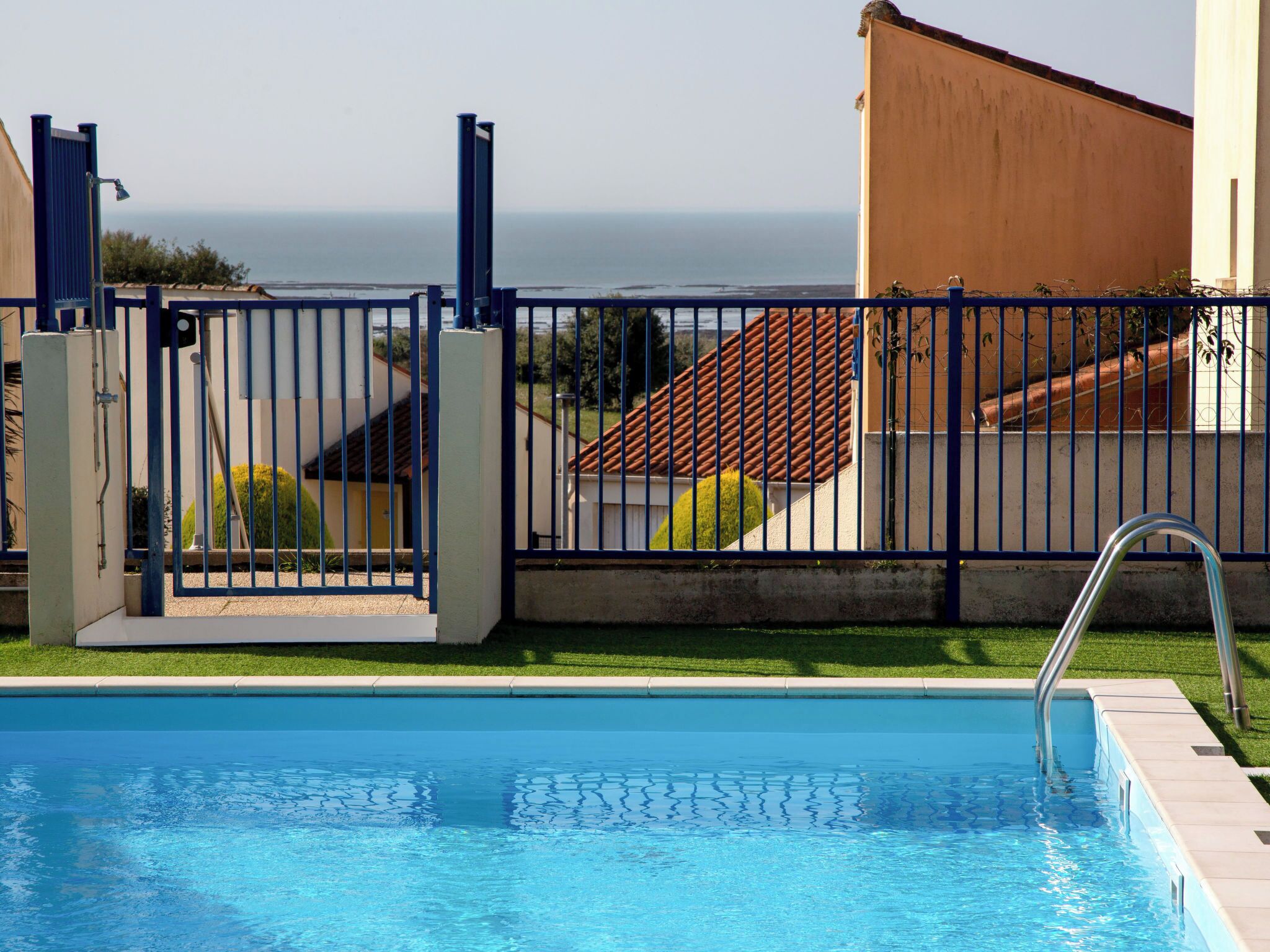 A swimming pool with a metal gate, a view of the sea, and a building with a tiled roof.